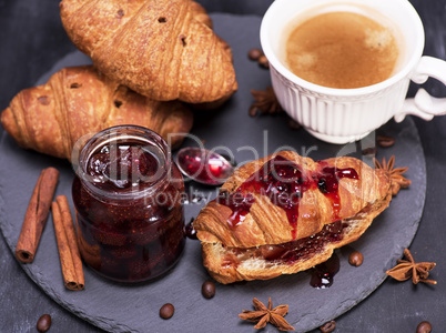 croissant with strawberry jam and white cup with coffee