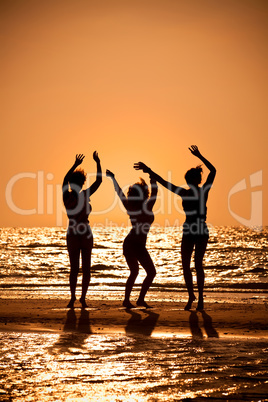 Three Young Women Dancing On Beach At Sunset