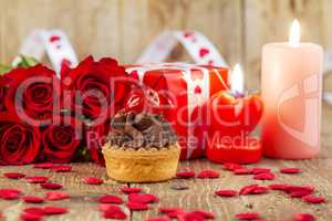 Cupcake with cherry in front of bouquet of red roses and cadles