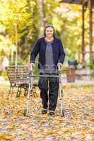Senior woman walking outdoors with walker in autumn park