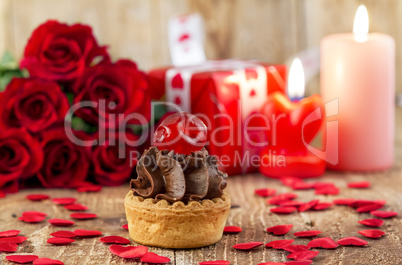 Cupcake with cherry in front of bouquet of red roses