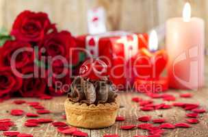 Cupcake with cherry in front of bouquet of red roses
