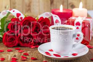 Cup with coffee in front of bouquet of red roses