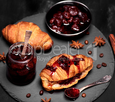strawberry jam in a glass jar and baked croissant