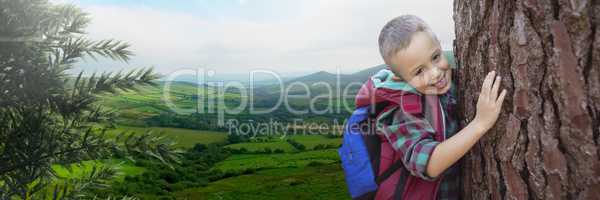 Travelling boy with bag in front of landscape holding tree