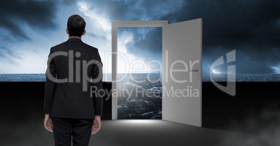 Businessman standing by open door with surreal dark sea glow and sky