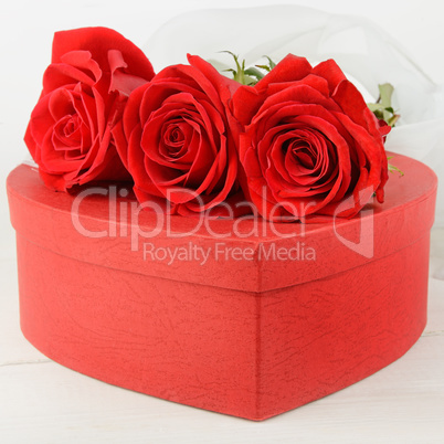 Gift box in the form of heart and scarlet roses on white wooden