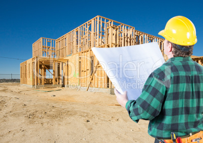 Contractor with Plans and Hard Hat Looking At New House Framing
