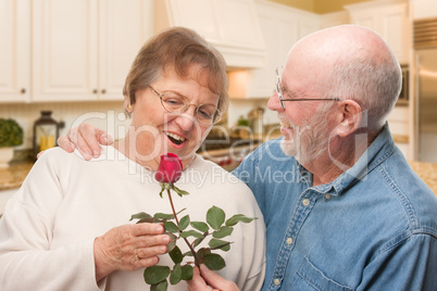Happy Senior Adult Man Giving Red Rose to His Wife Inside Kitche