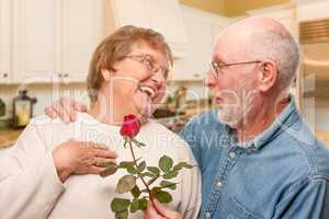 Happy Senior Adult Man Giving Red Rose to His Wife Inside Kitche