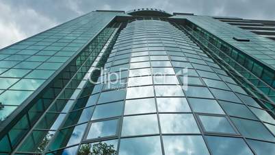 Time lapse, looking up at a glass-covered skyscraper, reflecting the blue sky and passing cloud