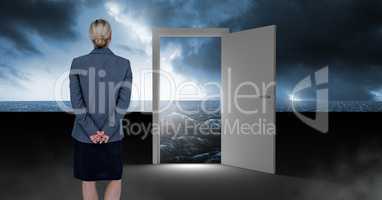 Businesswoman standing by open door with surreal dark sea glow and sky
