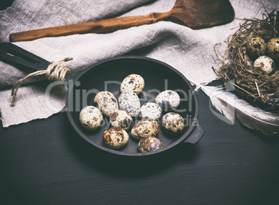 raw quail eggs in the shell lie in a black cast-iron frying pan