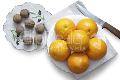 Oranges in the bowl and walnuts on a white background.