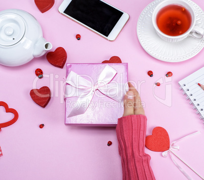 a female hand holds a pink box with a bow over the table