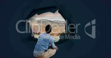Man looking through surreal paper hole at nature landscape