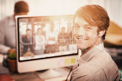 Composite image of happy businessman sitting at computer desk