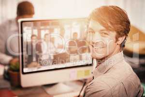 Composite image of happy businessman sitting at computer desk