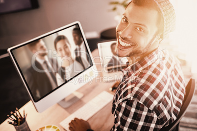 Composite image of portrait of man smiling while sitting by computer