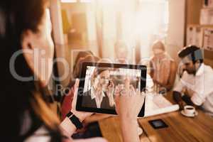 Composite image of businesswoman using digital tablet while discussing with colleagues