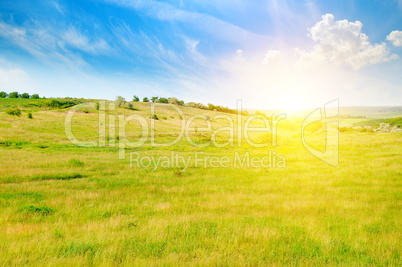 Hilly green fields and sunrise on a blue sky.