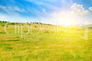 Hilly green fields and sunrise on a blue sky.