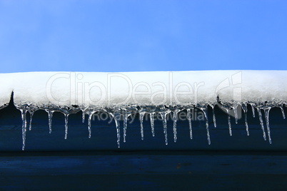 Icicles hang down from under the roof of the house. Frozen winter pattern