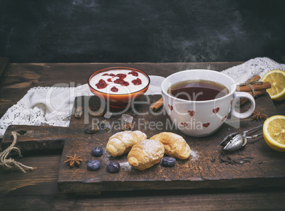 ceramic white cup with hot tea, croissants and yogurt