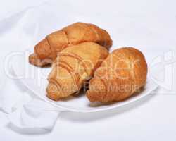 three freshly baked croissants on a white ceramic plate
