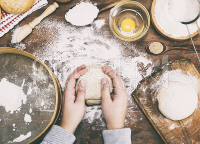 women's hands hold a ball of yeast dough on a table