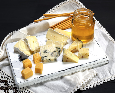 cheese board with various pieces of cheese and a glass jar with