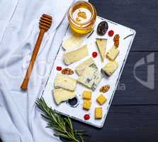 pieces of cheese on a white board and a glass jar with honey