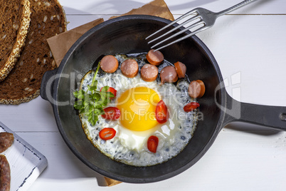 chicken egg with sausage slices in a round black cast-iron fryi