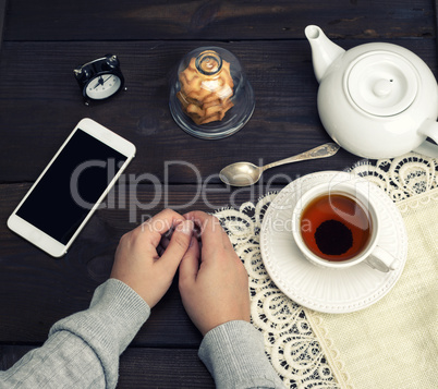female hands lie on a wooden table, next to a cup of tea and a s