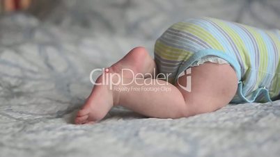 closeup panorama of baby's feet trying to crawl lying on the bed with blue and white blanket at day light