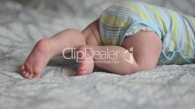 closeup panorama of baby's feet trying to crawl lying on the bed with blue and white blanket at day light
