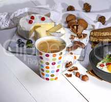 coffee with brown foam in a white ceramic mug, behind a round ca