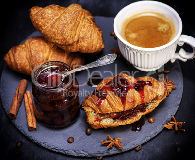 croissant with strawberry jam and white cup with coffee