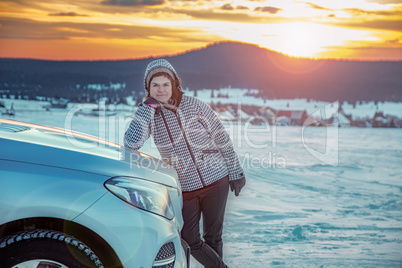 Woman at the car in snow landscape with sunset