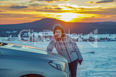 Woman at the car in snow landscape with sunset