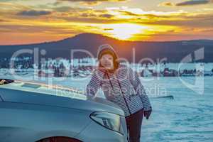 Woman at the car in snow landscape with sunset