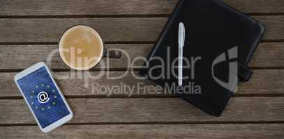 Composite image of mobile phone, coffee, pen and organizer on wooden plank