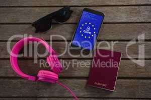 Composite image of headphones, sunglasses, passport and mobile phone wooden plank