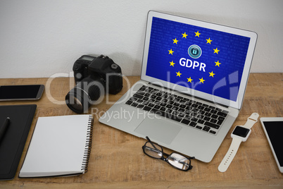 Composite image of laptop, wristwatch, notepad, camera and mobile phone on wooden table