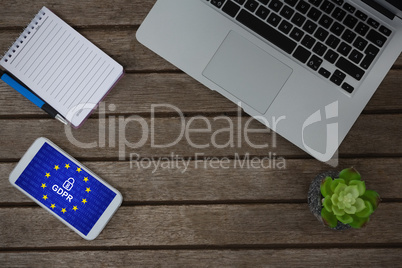 Composite image of laptop, pot plant, notepad, pen and mobile phone on wooden plank