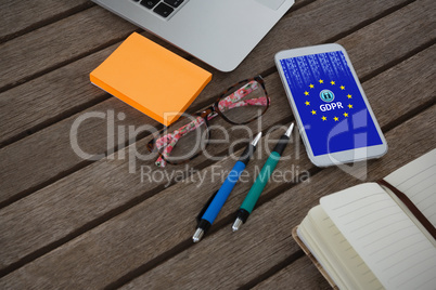 Composite image of mobile phone, laptop, pen, sticky note, spectacles and organizer on wooden plank