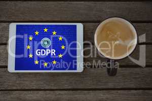 Composite image of digital tablet and cup of coffee on wooden plank