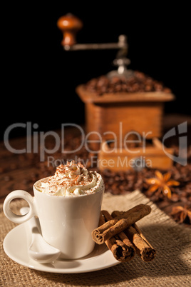 Coffee cup with whipped cream and coffee grinder on background