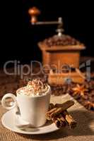 Coffee cup with whipped cream and coffee grinder on background