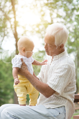 Grandfather holding grandson at outdoor bench.